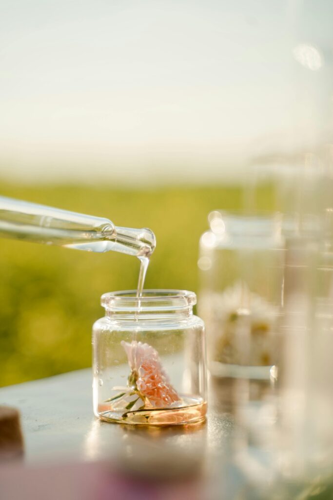 Close-up of a pipette adding liquid to a jar with a flower, outdoors in daylight.