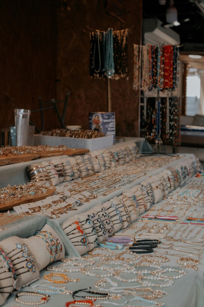 An array of handcrafted bracelets, necklaces, and jewelry displayed on tables in a market setting.