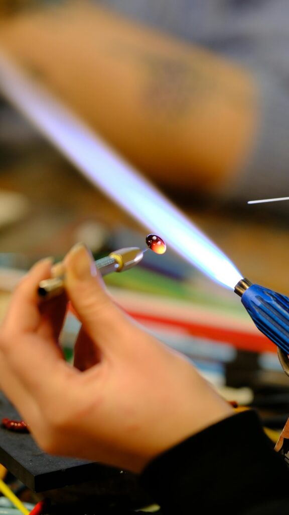 Detailed shot of a hand crafting glass bead using a flame torch.